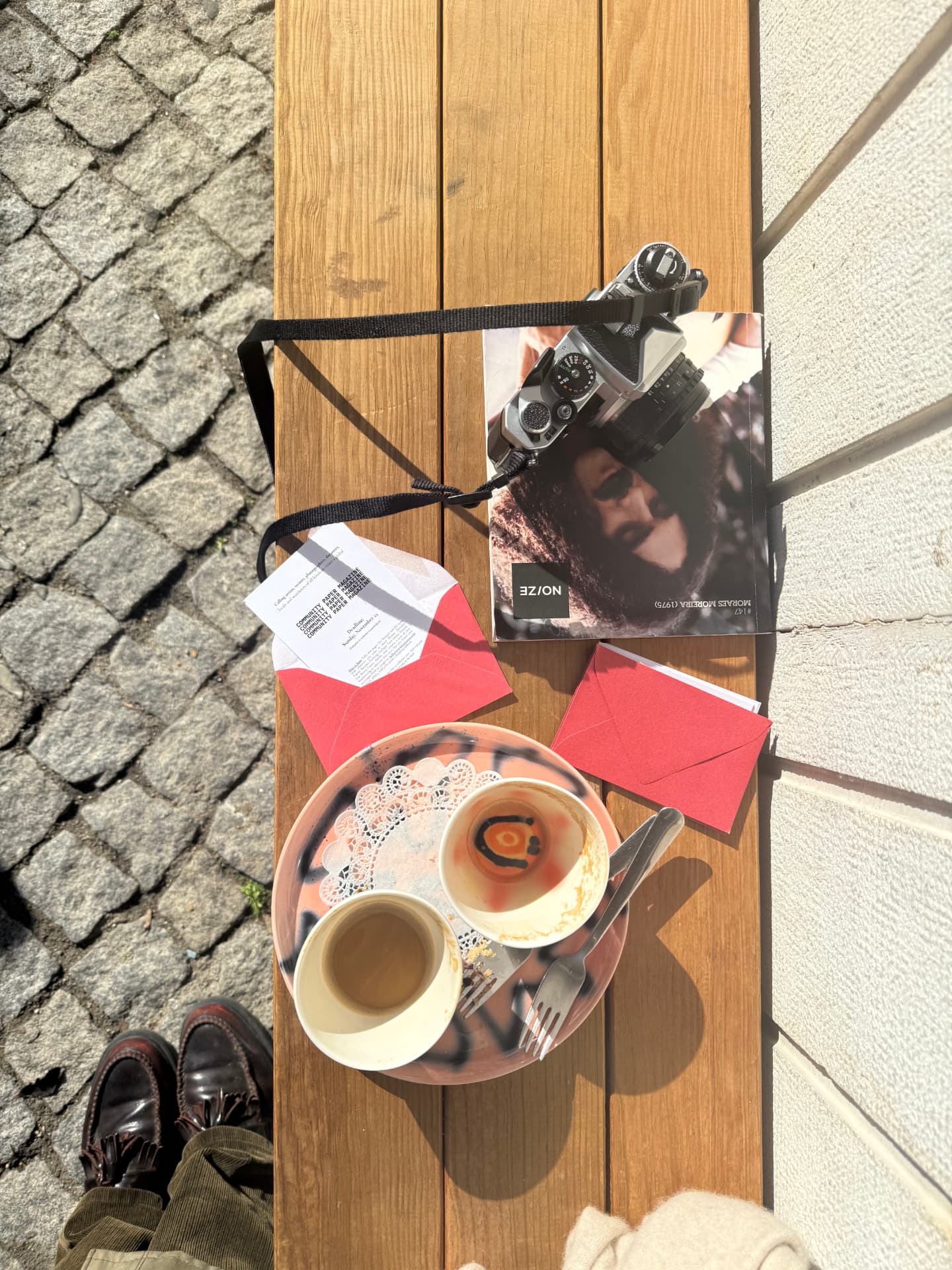 2Pages flyers, red envelopes and a copy of Issue 01 on a café table in the sun